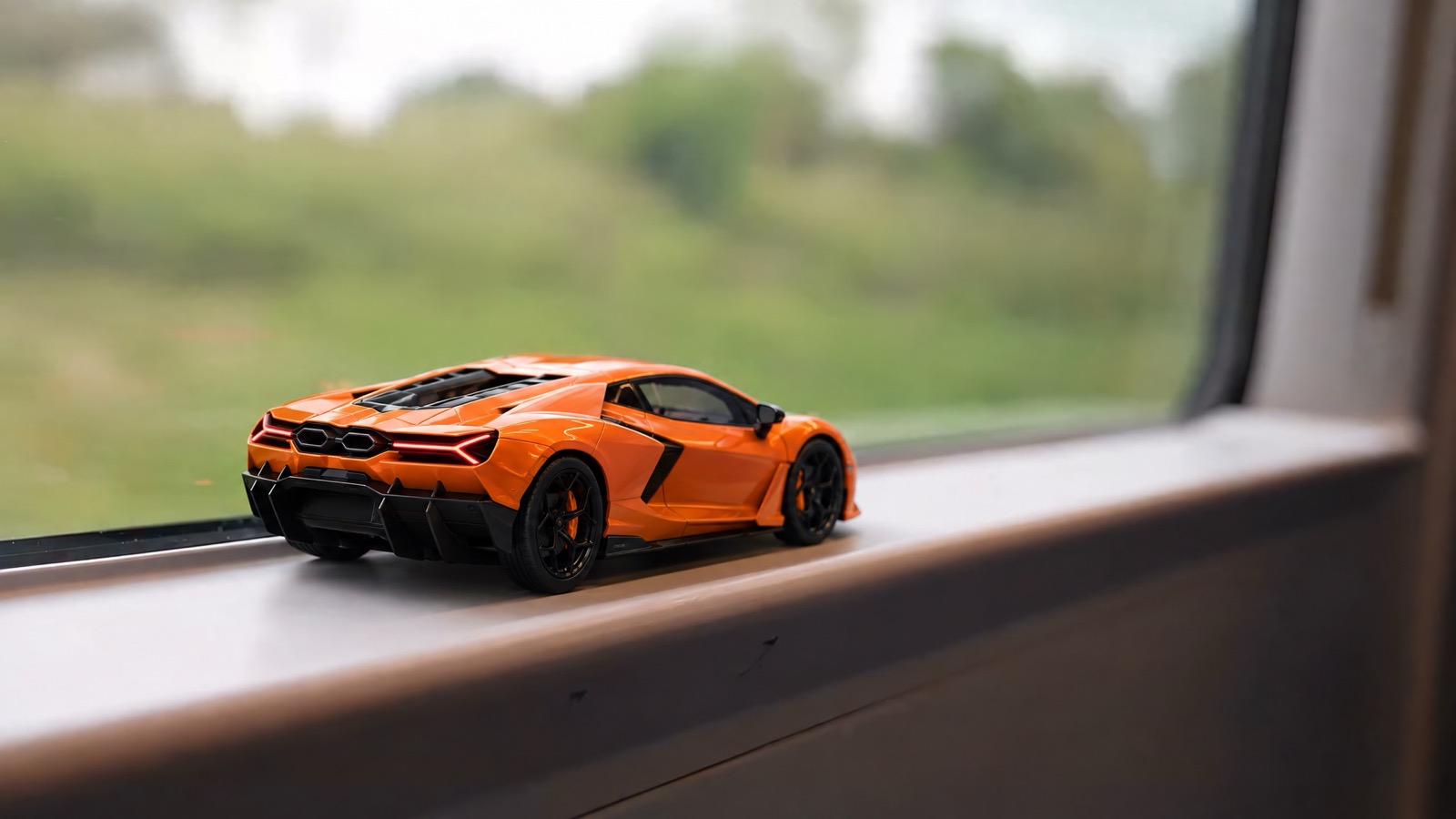 An orange Lamborghini Revuelto die-cast model on a train window ledge